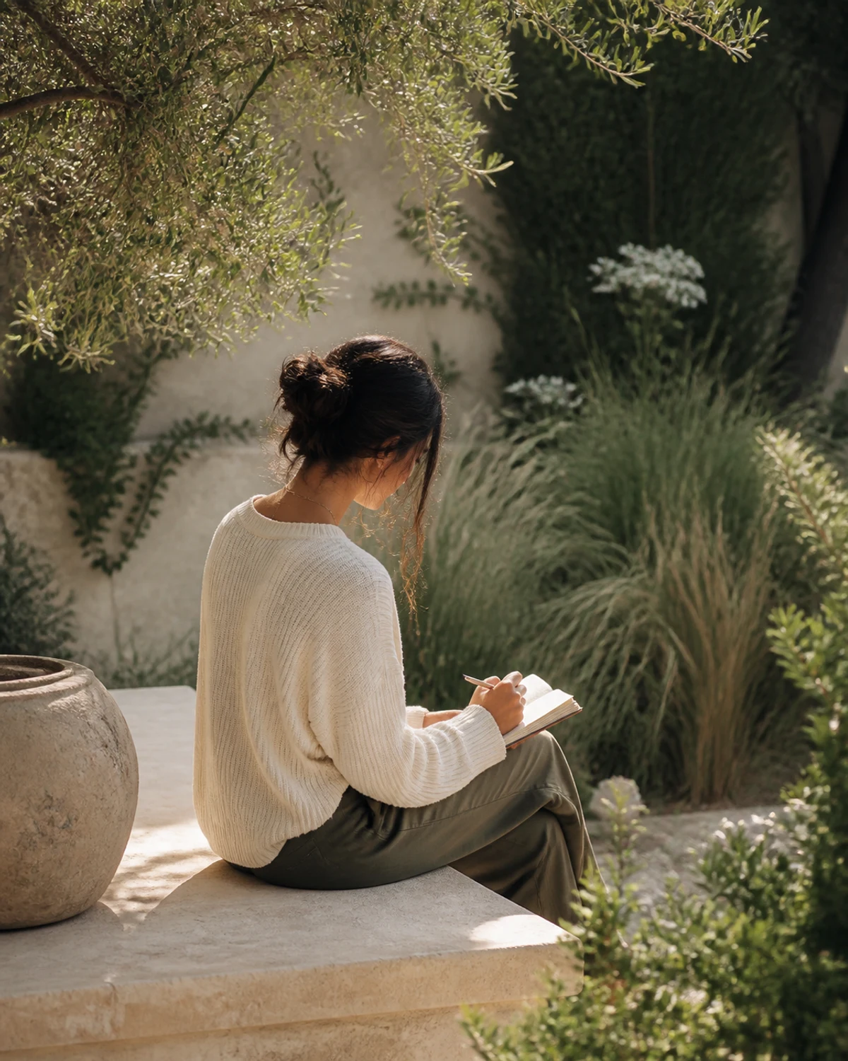 A person journaling in a sunlit botanical courtyard